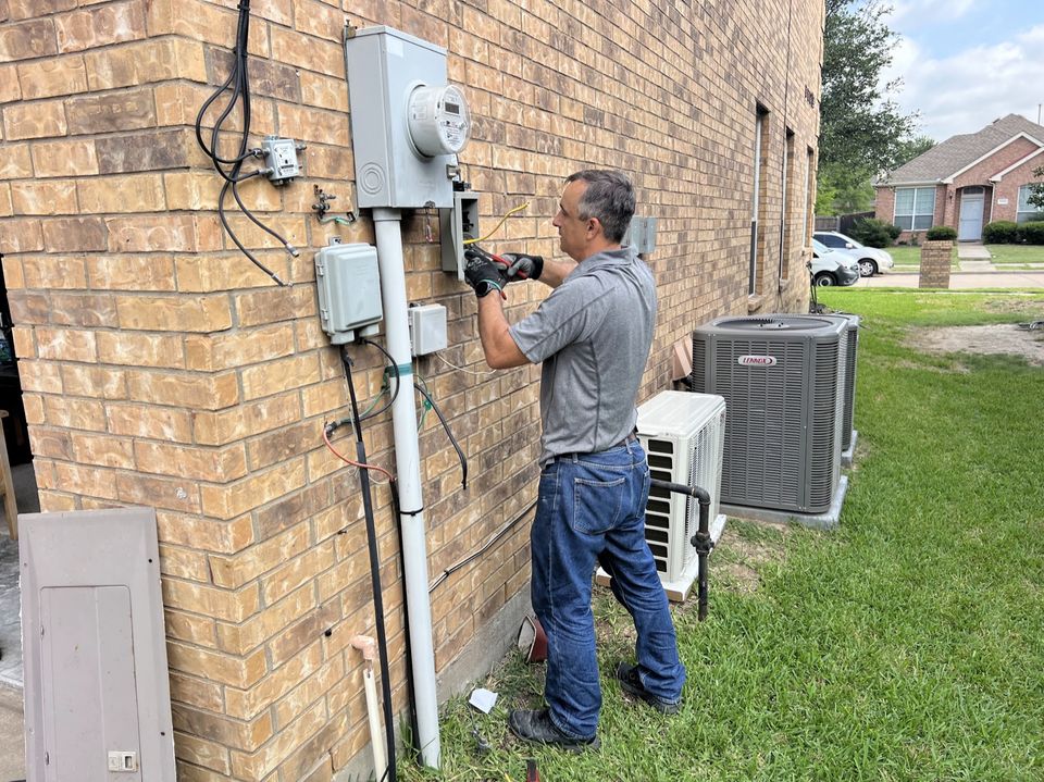 Technician checking the electrical disconnect and wiring beside an outdoor air conditioning unit