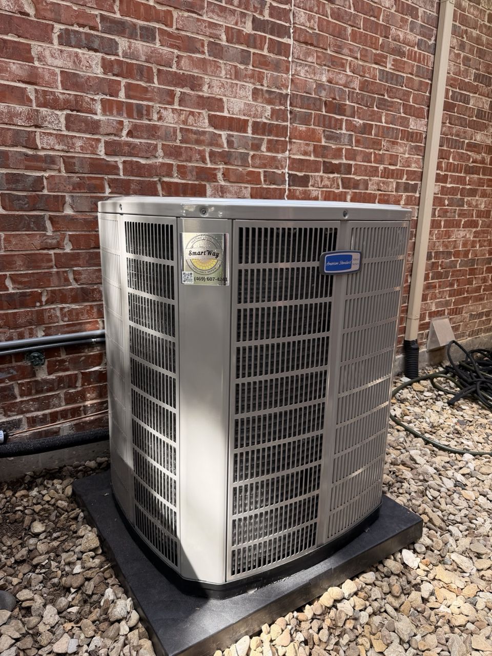 American Standard condenser with a SmartWay sticker on a pad beside a brick wall at a McKinney home