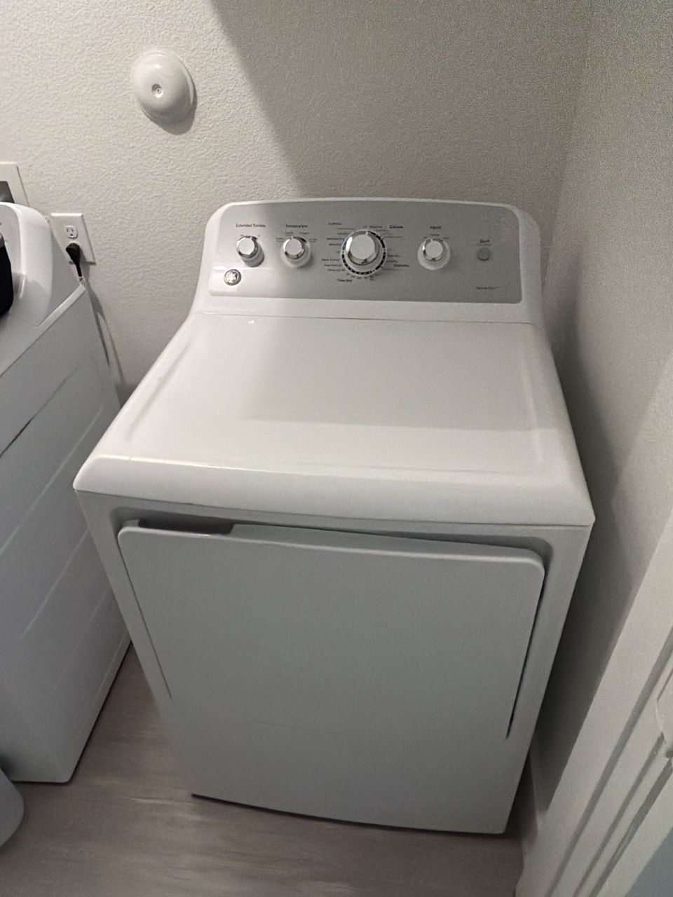 White GE dryer with dial controls standing next to the washer in a small laundry room