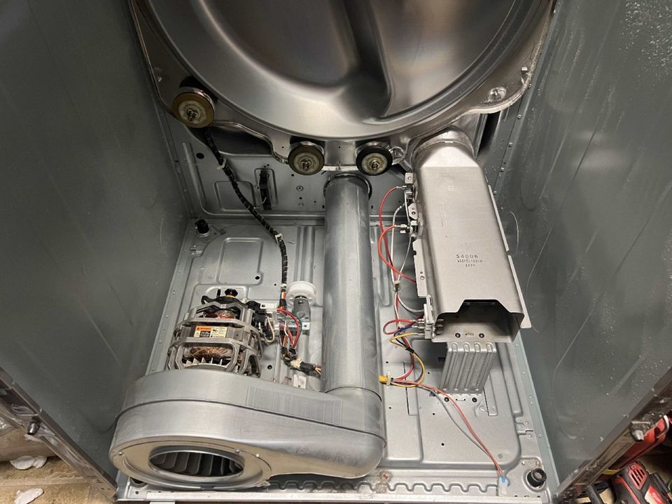 Dryer with the front panel off, showing the drum rollers, drive motor, blower housing and heating element housing