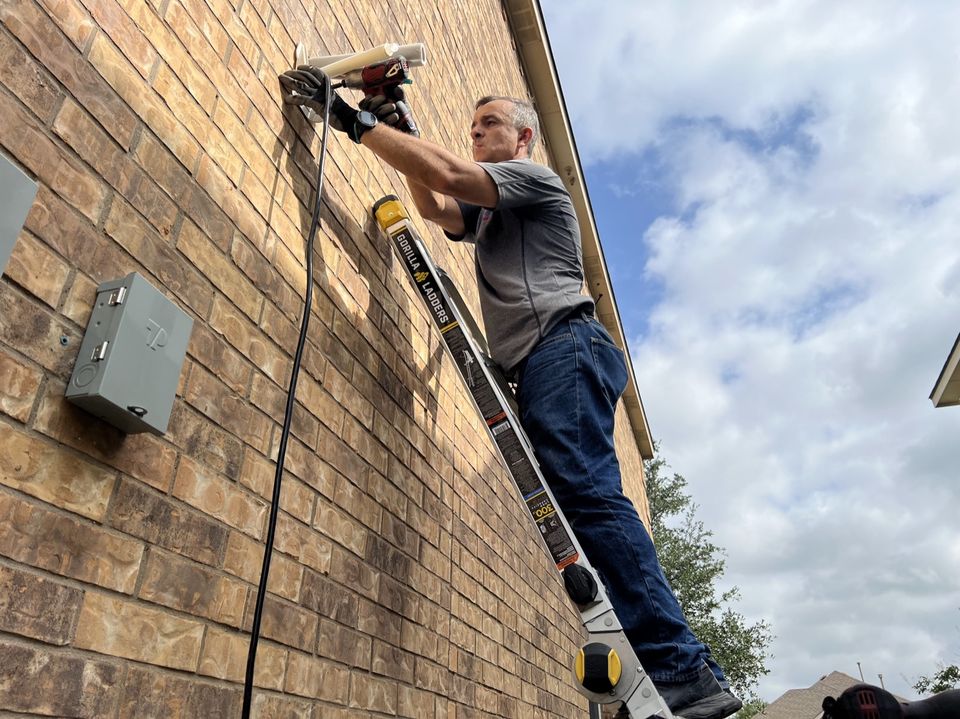 Technician on a ladder running a mini split line set up the outside wall of a house