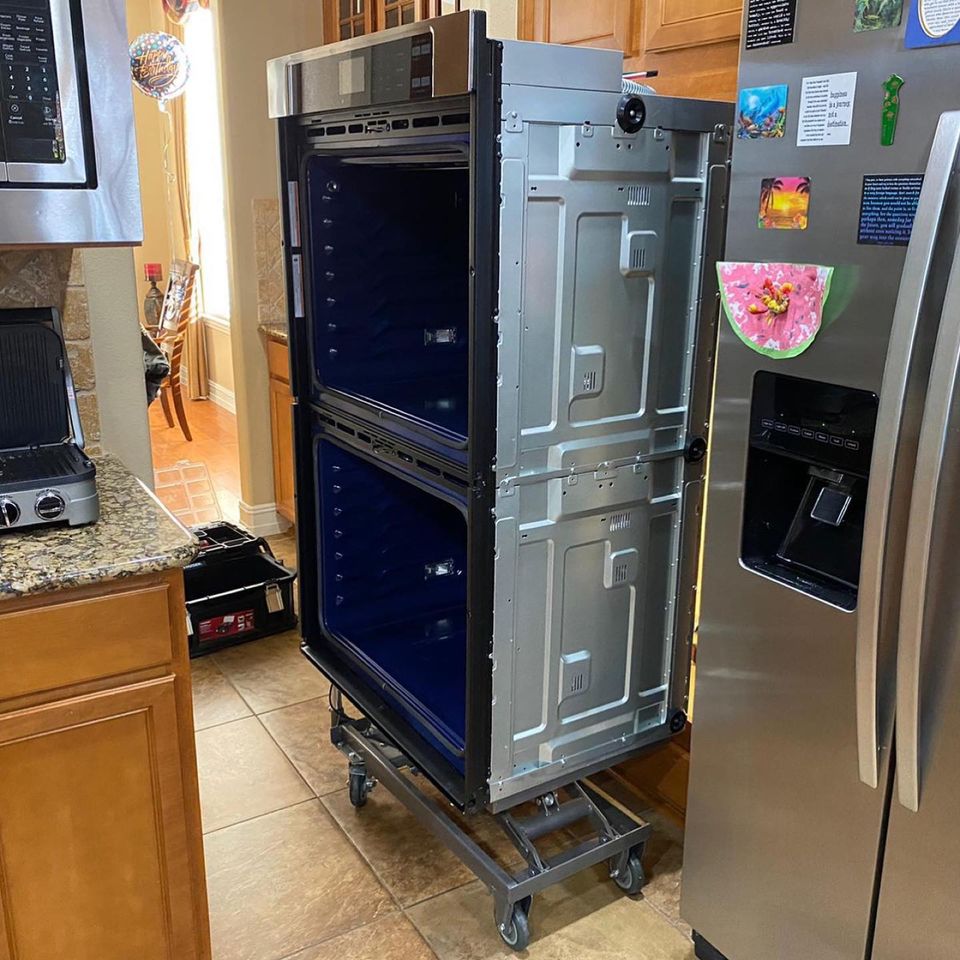 Stainless double wall oven pulled out of its kitchen cabinet and resting on a wheeled lift cart