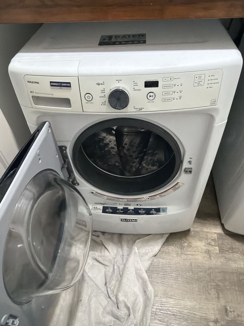 White Maytag Maxima front-load washer with its door swung open and a towel on the floor in front